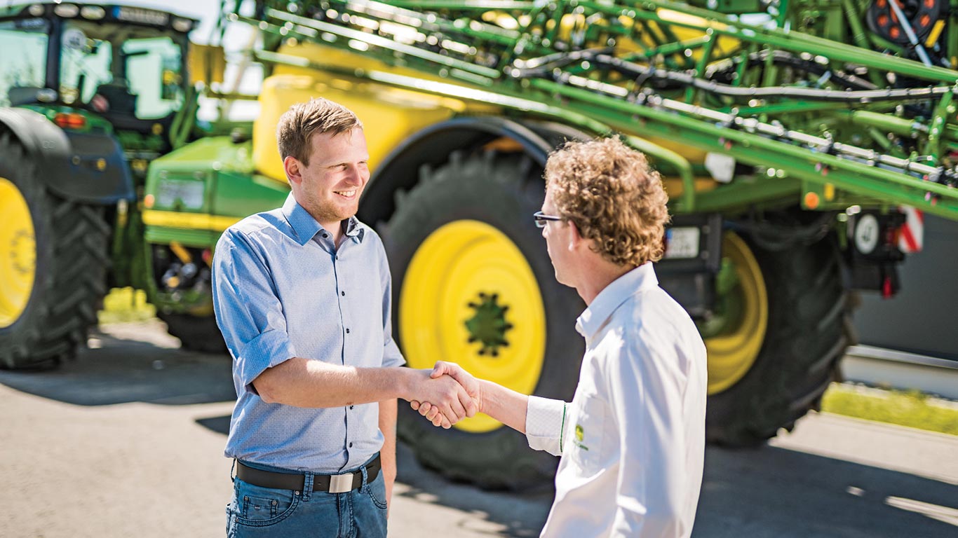 Håndtrykk forhandler og kunde foran John Deere sprøyte